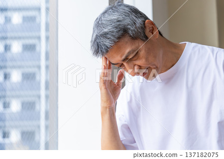 Senior man holding his head by the window Senior man holding his head by the window 137182075