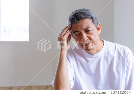 Senior man holding his head in the living room 137182094