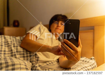 Mature sleepy woman lying in bed browsing social media on smartphone at night, insomnia, internet addiction Mature sleepy woman lying in bed browsing social media on smartphone at night, insomnia, internet addiction 137182597