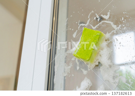 Green sponge cleaning glass shower door with soap suds in bathroom Green sponge cleaning glass shower door with soap suds in bathroom 137182613
