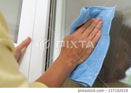 Adult woman washing glass window with blue cloth. Cleaning and professional house cleaning, small business Adult woman washing glass window with blue cloth. Cleaning and professional house cleaning, small business 137182618