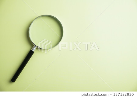 Black handled magnifying glass on a light green background. 137182930