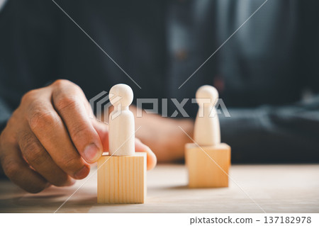 Hand places wooden figure on a block, symbolizing leadership, success, or team building. 137182978