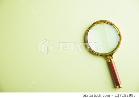 A gold-rimmed magnifying glass with a brown wooden handle, lying on a pale green background. A gold-rimmed magnifying glass with a brown wooden handle, lying on a pale green background. 137182993