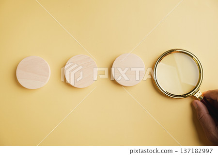 Three wooden circles on a yellow background, next to a magnifying glass. Three wooden circles on a yellow background, next to a magnifying glass. 137182997