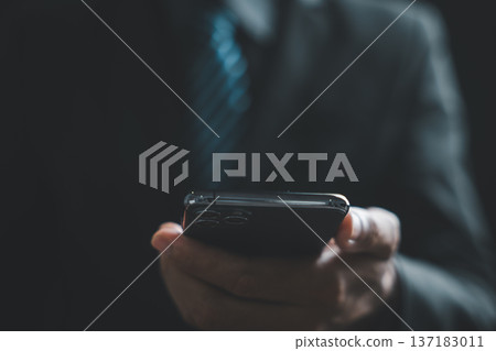 A blurry image of a hand holding a smartphone, with a blurred background of a person in a suit. A blurry image of a hand holding a smartphone, with a blurred background of a person in a suit. 137183011