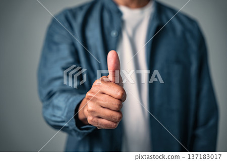A man posing with his hand makes a thumbs up sign, a good gesture and pose to show business success while holding a confident and professional pose for the camera in his studio 137183017