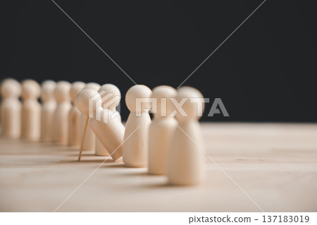A line of wooden figurines standing on a table, one is falling over. The figurines are out of focus except for the one falling, which is in focus. 137183019