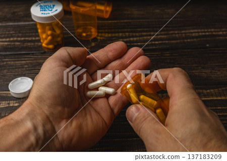 Man holds white and yellow pills while using a pill bottle Man holds white and yellow pills while using a pill bottle 137183209