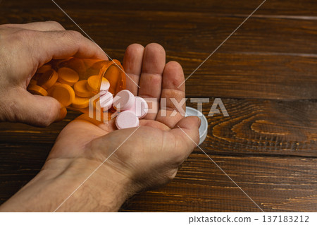 Hands holding a pill bottle and pouring tablets into a palm 137183212