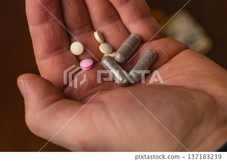 Hand holding different types of pills and capsules on a wooden surface Hand holding different types of pills and capsules on a wooden surface 137183239