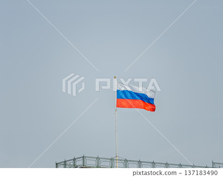 Russian tricolor flag waving in the wind against a blue sky. Russian tricolor flag waving in the wind against a blue sky. 137183490