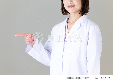 A middle-aged female doctor in a white coat pointing 137184606