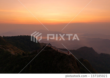 Aerial view of a mountain ridge path with a fence overlooking a breathtaking valley and sea of clouds at sunrise. 137185021