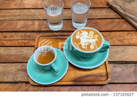 Beautiful unicorn latte art and a shot of espresso served on a wooden tray in a cafe. Beautiful unicorn latte art and a shot of espresso served on a wooden tray in a cafe. 137185027
