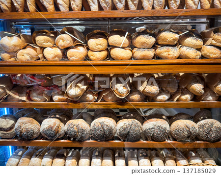 Freshly baked baguettes and artisan bread loaves displayed on wooden shelves in a bakery. Freshly baked baguettes and artisan bread loaves displayed on wooden shelves in a bakery. 137185029
