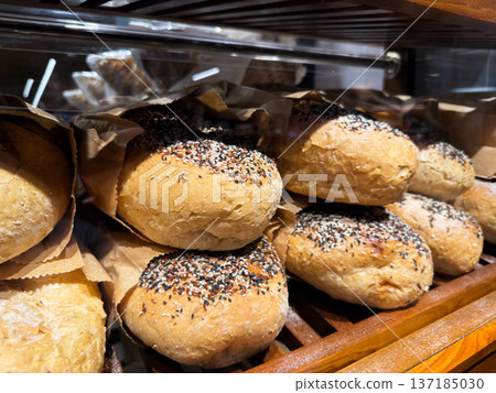 Close-up of freshly baked artisan bread rolls topped with mixed seeds in paper bags. Close-up of freshly baked artisan bread rolls topped with mixed seeds in paper bags. 137185030