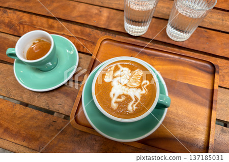 Beautiful unicorn latte art and a shot of espresso served on a wooden tray in a cafe. Beautiful unicorn latte art and a shot of espresso served on a wooden tray in a cafe. 137185031