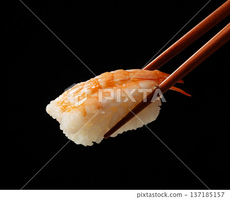 Shrimp sushi picked up with chopsticks on a black background 137185157