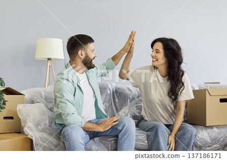 Smiling couple sharing a high five on sofa amid moving boxes in their new home Smiling couple sharing a high five on sofa amid moving boxes in their new home 137186171