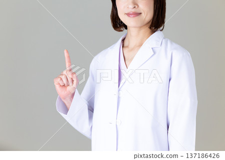 A middle-aged female doctor in a white coat pointing up A middle-aged female doctor in a white coat pointing up 137186426