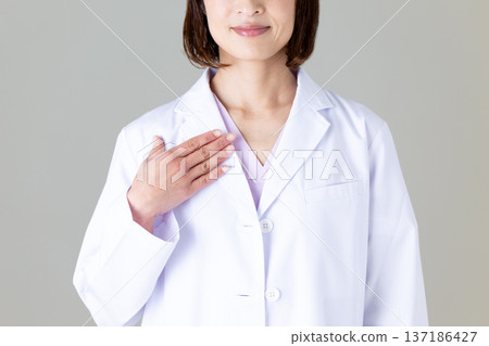 A middle-aged female doctor in a white coat holding her hand on her chest 137186427