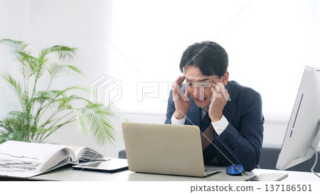 A male business person worried while working on a PC in the office A male business person worried while working on a PC in the office 137186501
