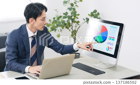 A male business person working while looking at a PC in the office 137186502