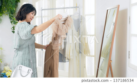 A woman choosing clothes while looking in the mirror at an apparel shop A woman choosing clothes while looking in the mirror at an apparel shop 137186534