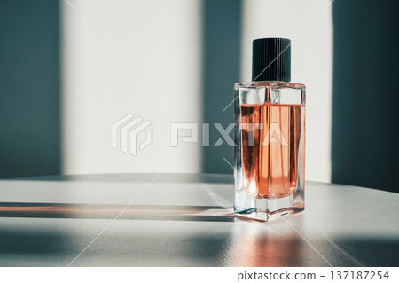 Clear glass perfume bottle containing orange liquid casting shadows on white surface 137187254