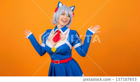 Happy young woman in blue anime cosplay costume with white wig and cat ears posing on orange background for japanese pop culture event Happy young woman in blue anime cosplay costume with white wig and cat ears posing on orange background for japanese pop culture event 137187653