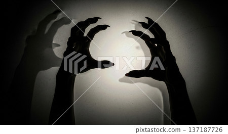 Spooky silhouette of scary witch hands with sharp claws grasping on dark wall background for Halloween horror concept, creepy zombie monster nightmare theme Spooky silhouette of scary witch hands with sharp claws grasping on dark wall background for Halloween horror concept, creepy zombie monster nightmare theme 137187726
