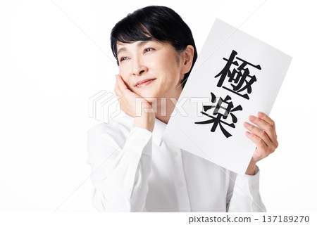 一位身穿白襯衫的老婦人面帶微笑，手裡拿著一張紙，上面寫著「天堂」二字。 137189270