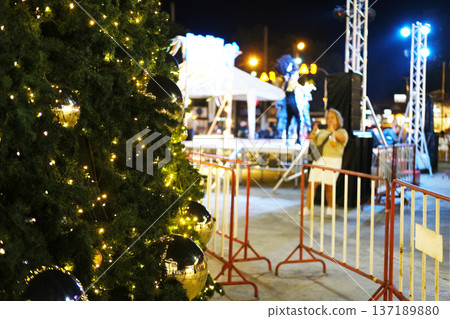 Christmas tree adorned with lights and ornaments stands in the square beside a stage, creating a festive atmosphere for holiday entertainment events Christmas tree adorned with lights and ornaments stands in the square beside a stage, creating a festive atmosphere for holiday entertainment events 137189880