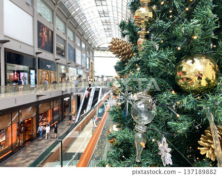 Christmas tree adorned with golden ornaments and decorations in a modern shopping mall, showcasing festive spirit and holiday shopping atmosphere Christmas tree adorned with golden ornaments and decorations in a modern shopping mall, showcasing festive spirit and holiday shopping atmosphere 137189882