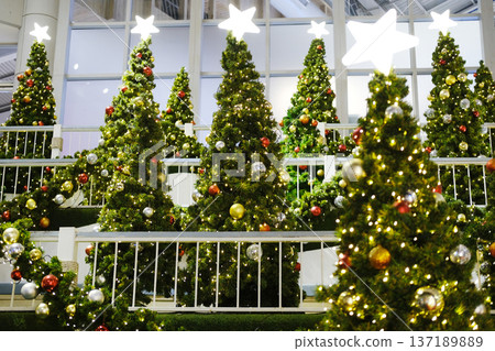 Festively decorated Christmas trees adorned with colorful ornaments and bright lights create a joyful atmosphere in a public space, enhancing the holiday spirit and inviting celebration Festively decorated Christmas trees adorned with colorful ornaments and bright lights create a joyful atmosphere in a public space, enhancing the holiday spirit and inviting celebration 137189889