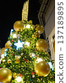Festive Christmas tree adorned with golden ornaments, sparkling lights, and a shimmering star on top, creating a joyful holiday atmosphere in a nighttime setting 137189895