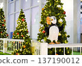 Festive decor featuring a whimsical bird statue surrounded by beautifully adorned Christmas trees, creating a joyful atmosphere in a public space for holiday celebrations 137190012