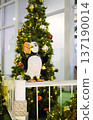 Festive Christmas decor featuring a whimsical bird sculpture beside a beautifully adorned tree, creating a joyful atmosphere in a public space with twinkling lights and vibrant ornaments 137190014