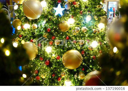 Festive Christmas tree adorned with golden and red ornaments, twinkling lights, and a star on top, creating a warm holiday atmosphere and joyful ambiance Festive Christmas tree adorned with golden and red ornaments, twinkling lights, and a star on top, creating a warm holiday atmosphere and joyful ambiance 137190016