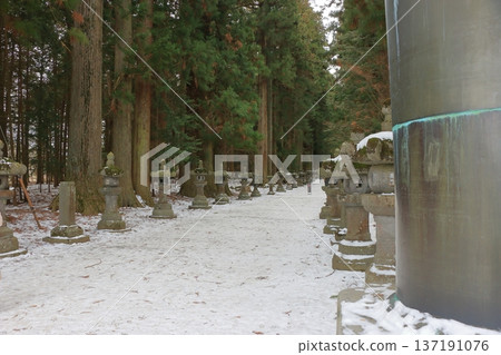 The long pathway to the Kitaguchi Hongu Sengen Jinja shrine, the entrance to the path to climb Mt. Fuji, lined with stone lanterns in Fujiyoshida in Yamanashi Japan on a snow covered winter day. The long pathway to the Kitaguchi Hongu Sengen Jinja shrine, the entrance to the path to climb Mt. Fuji, lined with stone lanterns in Fujiyoshida in Yamanashi Japan on a snow covered winter day. 137191076