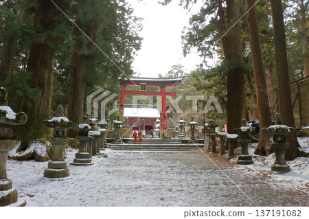 The long pathway to the Kitaguchi Hongu Sengen Jinja shrine, the entrance to the path to climb Mt. Fuji, lined with stone lanterns in Fujiyoshida in Yamanashi Japan on a snow covered winter day. The long pathway to the Kitaguchi Hongu Sengen Jinja shrine, the entrance to the path to climb Mt. Fuji, lined with stone lanterns in Fujiyoshida in Yamanashi Japan on a snow covered winter day. 137191082