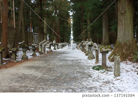 The long pathway to the Kitaguchi Hongu Sengen Jinja shrine, the entrance to the path to climb Mt. Fuji, lined with stone lanterns in Fujiyoshida in Yamanashi Japan on a snow covered winter day. The long pathway to the Kitaguchi Hongu Sengen Jinja shrine, the entrance to the path to climb Mt. Fuji, lined with stone lanterns in Fujiyoshida in Yamanashi Japan on a snow covered winter day. 137191084