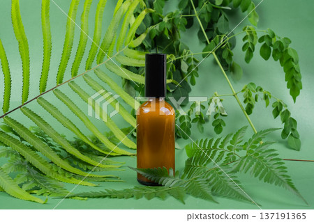 Glass bottles of toner and serum with leaves on green background. Beauty product packaging display Glass bottles of toner and serum with leaves on green background. Beauty product packaging display 137191365