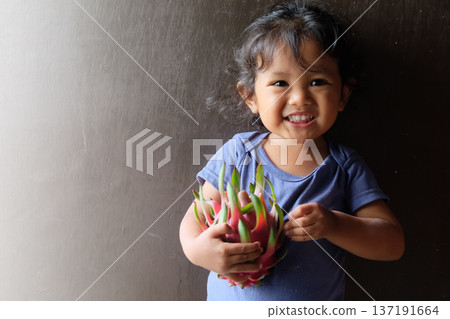 Close-up of cute curly boy enjoying exotic dragon fruit with red smudged face 137191664