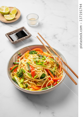 Vegetarian wok noodles with vegetables in a plate on a light marble background with chopsticks Vegetarian wok noodles with vegetables in a plate on a light marble background with chopsticks 137191744
