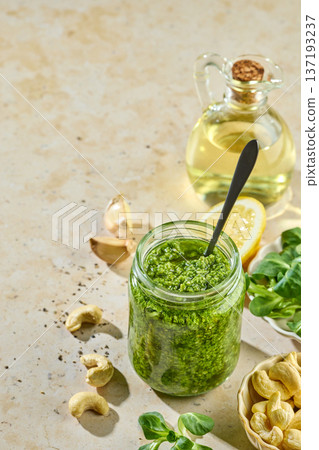 Fresh homemade green sprout pesto in glass jar on sunny kitchen table with ingredients Fresh homemade green sprout pesto in glass jar on sunny kitchen table with ingredients 137193237