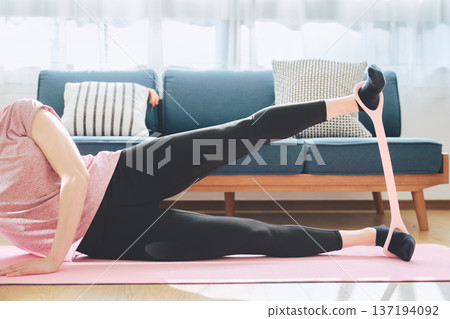 一名女子在瑜珈墊上使用訓練管進行下半身訓練。 一名女子在瑜珈墊上使用訓練管進行下半身訓練。 137194092