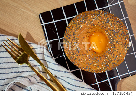 Seeded bagel with egg yolk on grid cutting board top view Seeded bagel with egg yolk on grid cutting board top view 137195454