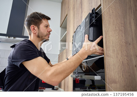 Man installing built in microwave oven in modern kitchen cabimet Man installing built in microwave oven in modern kitchen cabimet 137195456